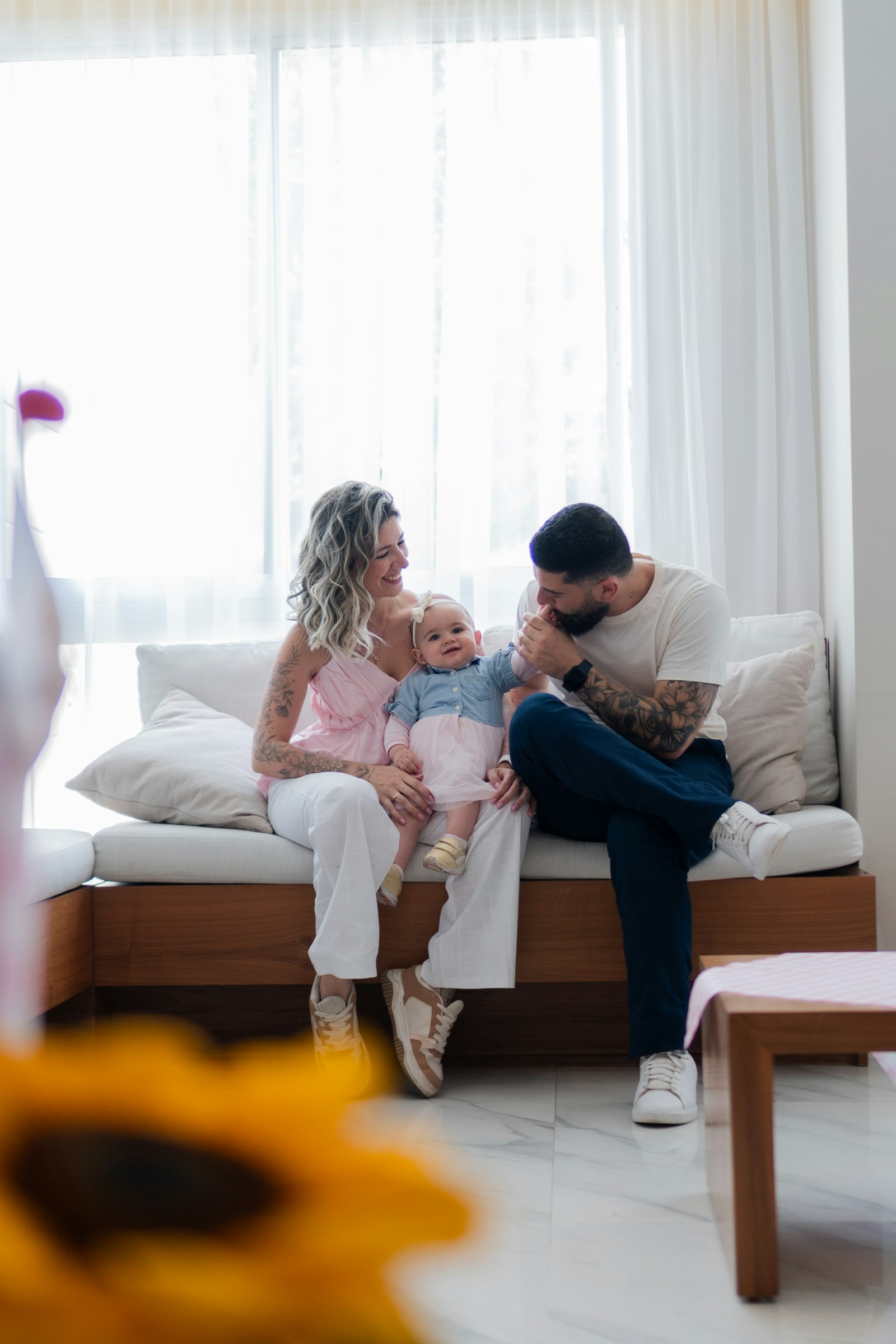 A mother, father and baby sitting together on a sofa in a bright room